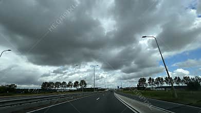 Curving motorway beneath dramatic storm clouds with sparse traffic, tall