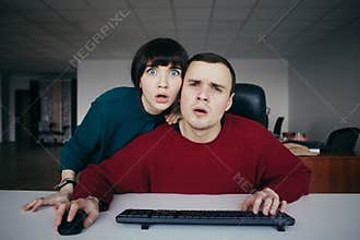 Surprised young beautiful people emotionally office workers looking at a computer screen. The situation in the office