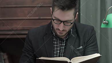 Young academic in glasses attentively reading a book