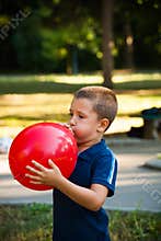 Little boy inflate big red balloon in park