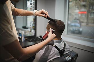 A stylish hairstylist serving client on a barbershop background. Hairdresser`s hands shaving male client`s head. Beauty