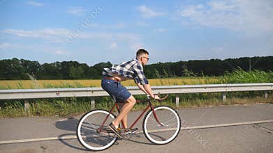 Young handsome man riding at vintage bicycle in the country road. Sporty guy cycling at the track. Male cyclist riding