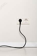 Black power cord cable plugged into european wall outlet on whit