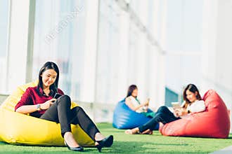 Group of Asian college student or business colleague using smartphone sit together in modern office or university campus