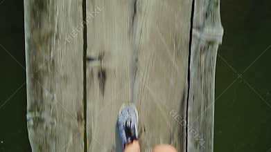 POV video: The feet of a woman are walking along a narrow wooden bridge over a mountain river. Danger and adventure