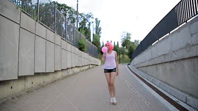 Steadicam shot of mixed race trendy hipster teenage girl walking and blowing a red balloon wearing pink wig