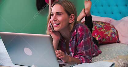 Woman Lying On Bed At Home Using Laptop And Answering Phone