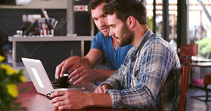 Two Men In Cafe Working On Laptop Together
