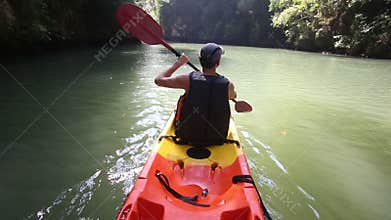 old man paddles on kayak down river among sun light and cliffs