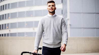 Young man walking along city street with bicycle