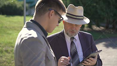 Two business partners speaking and using tablets outdoors. 4K