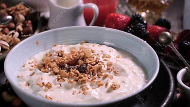 Pouring cereals over a bowl of yogurt for breakfast with berries and dry fruits