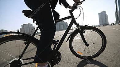 A man in a suit and shoes starts moving on a bicycle in a city in sunny weather.