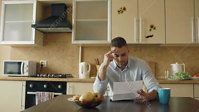 Upset young man reading letter with unpaid bill in the kitchen at home