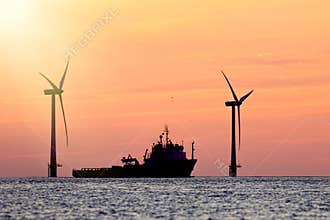 Sustainable resources. Wind farm with ship silhouette at tropical sunrise or sunset. Solar and wind energy and food supply
