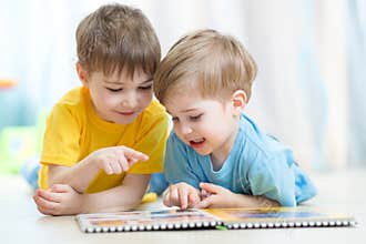 Kids brothers practice read together looking at book laying on the floor