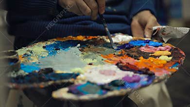 Artist mixes oil paints on pallet with various colors