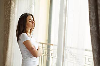 Portrait of a beautiful woman staying near the window and very seriously thinking about life.