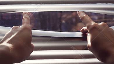 Female hand separating slats of venetian blinds with a finger to see through