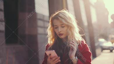 Worried business woman in red coat goes near business centre in the city, using Mobile Phone app. Steady cam shot.