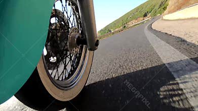 Motorcycle ride on a winding coastal road seen from the front wheel. Sardinia
