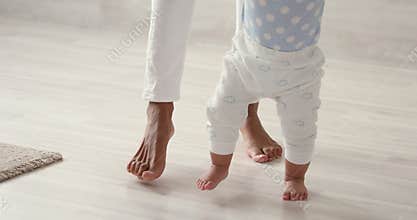 Barefoot little african american kid toddler learning walking with mom.