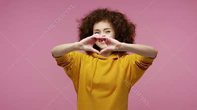 Be my Valentine! Cute happy girl afro hairstyle in hoodie making heart shape with hands and kissing air