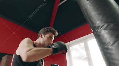Boxer man kicking combat bag in gym low angle view.