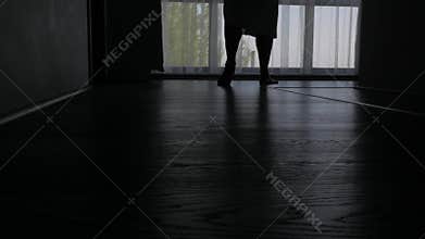 The silhouette of a man walking barefoot to a large window in a hotel room. Close-up of bare feet on the floor.