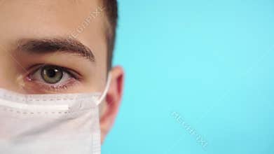 Young man puts on a facial medical mask on a blue background
