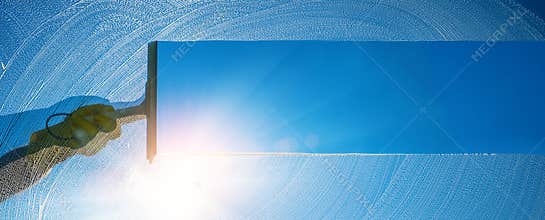 Window cleaner cleaning window with squeegee and wiper on a sunny day with a bright blue sky