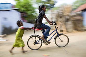 One young girl enjoy riding bicycle, another little girl holding and following her