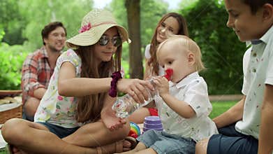 Family sitting on blanket in park. Adorable toddler drinking water from bottle