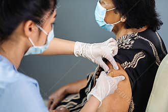 Doctor holding syringe and making injection to senior patient in medical mask. Covid-19 or coronavirus vaccine