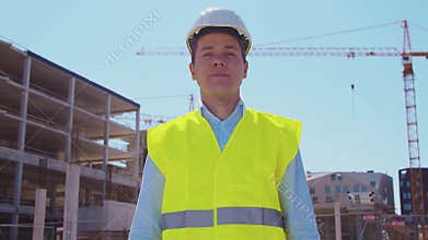 Professional builder standing in front of construction site. Foreman in hardhat helmet and vest. Office building and