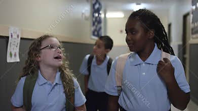 Black and white girls talk and laugh in school hall on the way to class.