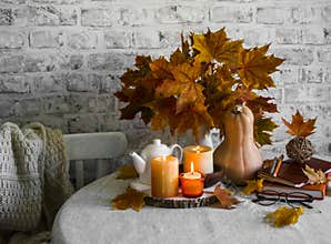 Lit candles, dry maple leaves, pumpkin, stack of books - autumn still life interior decoration house. Cozy home concept