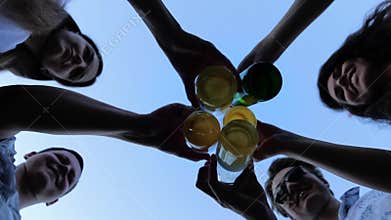 Bottom view: five friends clink with beer bottles against the sky on summer party