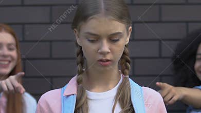 Cruel teenagers pointing fingers at upset girl, mocking nerd, discrimination