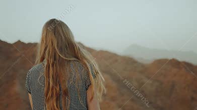 Young blond woman in long dress walks on top of mountain. Mountain landscape with sunset, slow motion, full hd