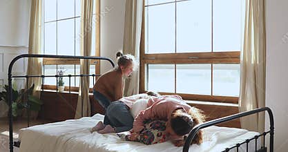 Carefree young woman fighting pillows with children in bedroom.