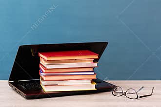 A stack of books lies in an open laptop and glasses on the table. Distance learning. The concept of choosing classical education