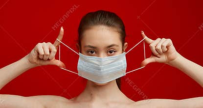 A young girl puts on a medical mask on a red background. Poster about the coronavirus COVID-19 pandemic.