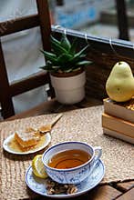 Morning setup on wooden table at balcony for morning relaxation with books, cup of tea, teapot, organic honey, green tea leaves