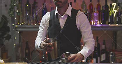 Professional barman in a white shirt and black apron throwing liquid with steel shaker. Shot in RED camera 4K in slow
