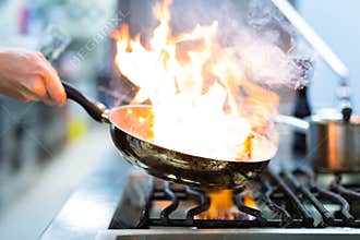 Chef in restaurant kitchen at stove with pan