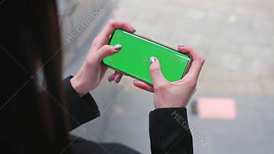 Close up hand woman young holding using touch smart phone with horizontal green screen play games background urban city
