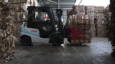 Loader carries waste paper while truck stands in warehouse