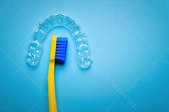 a bright toothbrush in yellow with plastic new braces lies on a blue background, no people