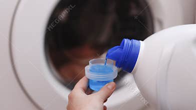 Close up shot of a woman hands squeezing liquid gel laundry detergent from a plastic bottle into a small container, with